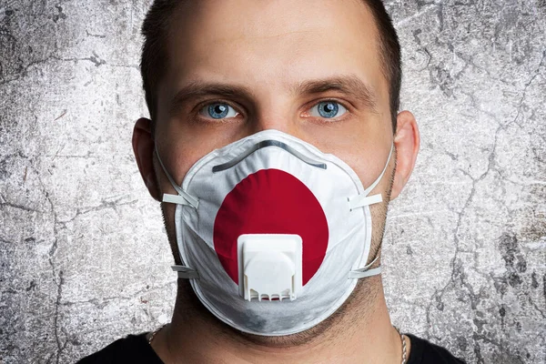 Young man with sore eyes in a medical mask painted in the colors of the national flag of Japan. Coronovirus disease  COVID-19 concept.  Man is afraid of getting the flu