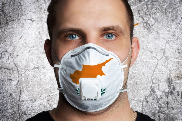 Young man with sore eyes in a medical mask painted in the colors of the national flag of Cyprus. Coronovirus disease  COVID-19 concept.  Man is afraid of getting the flu
