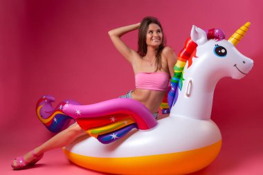 Yaz moda güzel kadın yaz giysileri eğlenmek, gülümseme ve balon ile poz üzerinde Unicorn float izole pembe arka plan
