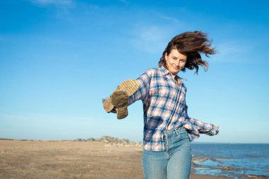 Neşeli, siyah saçlı bir kadın gülümser, kumsalda yürür, yaz gününde parlak güneşin tadını çıkarır. Denizde yaz tatili ve yaşam tarzı kavramı
