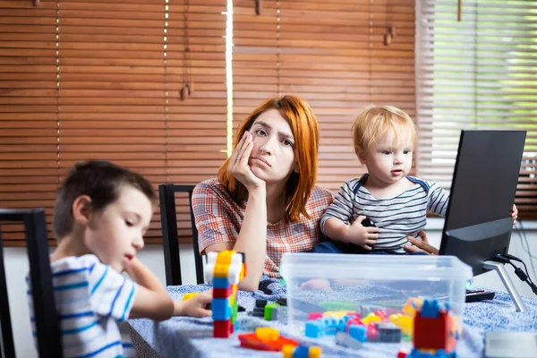 膝の上に男の子が二人いるお母さんは家で笑おうとする 若い女性は子供の世話をし コンピュータ上で動作します オンラインで仕事をし 同時に子供を育てる — ストック写真