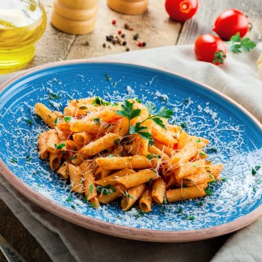 Geleneksel penne makarna sıcak arrabiata domates sosu ve rustik ahşap bir masa üzerine maydanoz ile. Geleneksel İtalyan sağlıklı gıda mavi tabakta. Üstten Görünüm.