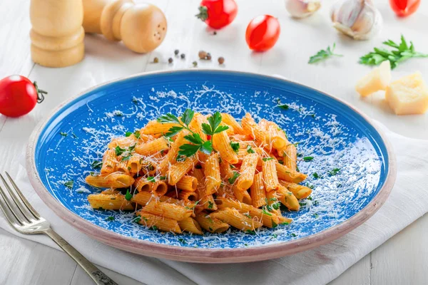 Mavi bir rustik tabakta domates soslu lezzetli İtalyan penne makarna. Beyaz ahşap bir masa üzerinde sağlıklı lezzetli İtalyan yemekleri.