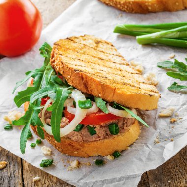 Lezzetli sandviç tost, ton balığı, domates, soğan ve roka bir tabloda malzemelerle yapılmış. Geleneksel sağlıklı gıda.
