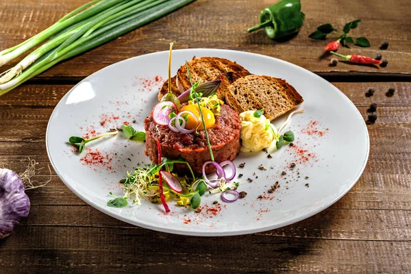 Gurme tartar, kızarmış ekmek ve tabakta salata. Köy ahşap bir masada çiğ etten yapılmış lezzetli sağlıklı Fransız mutfağı yemeği..
