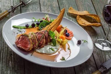 Orta pişmiş biftek, sos ve salata ile ahşap bir masada. Et filetosu ve taze sebzeden yapılmış sağlıklı gurme yemekleri..