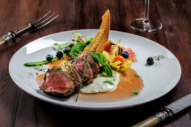 Lezzetli, orta pişmiş, soslu biftek ve tabakta salata. Tahta bir masada taze otlar ve şarapla et filetosundan yapılmış sağlıklı yiyecekler..