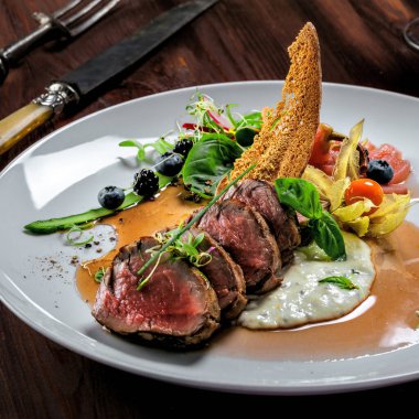 Lezzetli, orta pişmiş, soslu biftek ve tabakta salata. Et filetosundan yapılmış sağlıklı yiyecekler ve ahşap bir masada taze otlar..