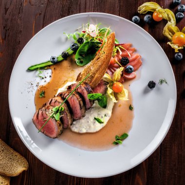 Lezzetli, orta pişmiş, soslu biftek ve tabakta salata. Et filetosundan yapılmış sağlıklı yiyecekler ve ahşap bir masada taze otlar. Üst görünüm.