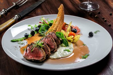 Lezzetli, orta pişmiş, soslu biftek ve tabakta salata. Et filetosundan yapılmış sağlıklı yiyecekler ve ahşap bir masada taze otlar..