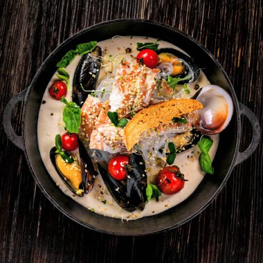 Krema soslu deniz ürünleri ve pirinç eriştesi. Deniz levreği, midye, yengeç eti ve domatesli ve pirinç erişteli diğer deniz ürünlerinden yapılmış sağlıklı bir yemek. Üst görünüm.