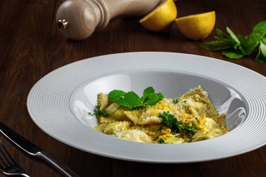 İtalyan mantısı makarna hamuru, ricotta, nane ve rendelenmiş limon koyu kahverengi ahşap bir masada çorba tabağında servis edilir..