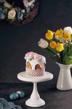 Beyaz ahşap tezgahta ev yapımı Paskalya pastası nergis buketi ve karanlık arka planda vazoda laleler. Tatil dekorasyonu kavramı.