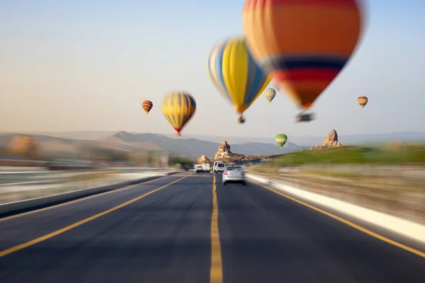 Globos de aire caliente vuela sobre la carretera al amanecer en Kapadokya, Turke —  Fotos de Stock