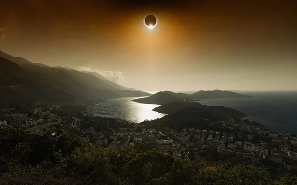 Eclipse solar total en el cielo brillante rojo oscuro sobre la ciudad costera —  Fotos de Stock