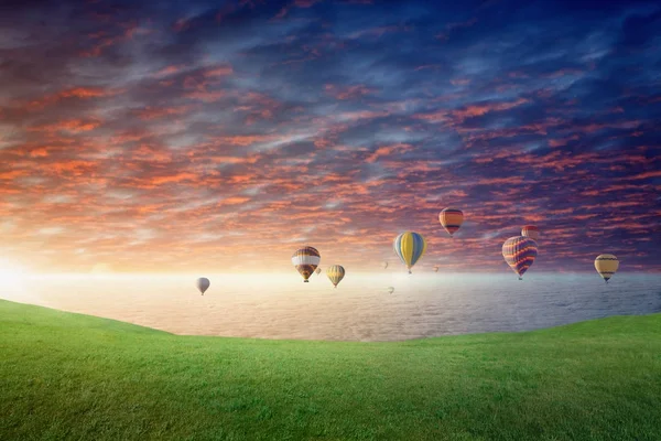 Heißluftballons fliegen im glühenden Sonnenuntergangshimmel über der grünen Wiese Stockbild