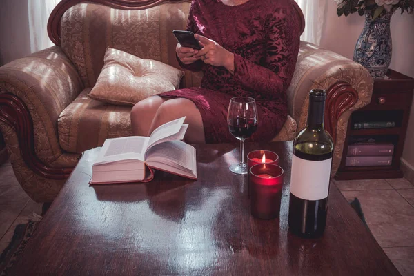 Mulher textando e usando um laptop com vinho em um livro de casa na mesa e velas — Fotografia de Stock