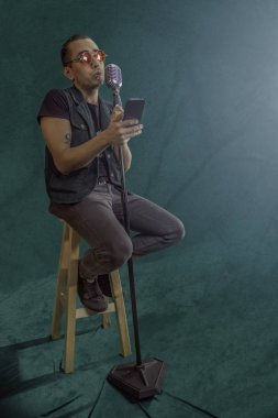 Rock yıldızlı Latin şarkıcı arka plandaki eski mikrofonun önünde cep telefonuna bakıyor.