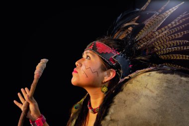 close up of young woman Teotihuacana, Xicalanca - Toltec in black background, with traditional dress dance with a trappings with feathers and drum