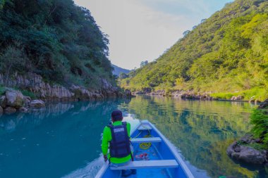 TAMUL, SAN LUIS POTOSI MEXICO - January 6, 2020: Rear view of man in raincoat and vest rowing in canoe. Active, adventure, outdoors, in tamul river