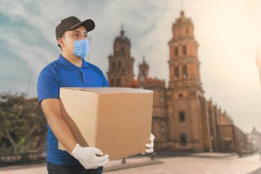 Ev teslimatı, online sipariş. Üniformalı bir adam, tıbbi bir maske ve kutulu lastik eldivenler, elinde bir paket, Meksika sokaklarında.