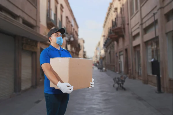 宅配便オンライン注文 メキシコの通りにある彼の手の中に箱と小包を持った制服を着た男医療マスクとゴム手袋 — ストック写真