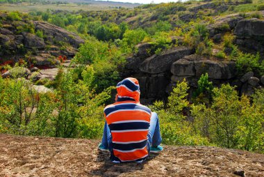 Parlak bir çizgili ceketli çocuk kayanın üzerinde oturuyor.