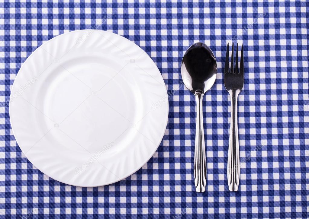 Empy plate and with a spoon fork on the tablecloth in a cage