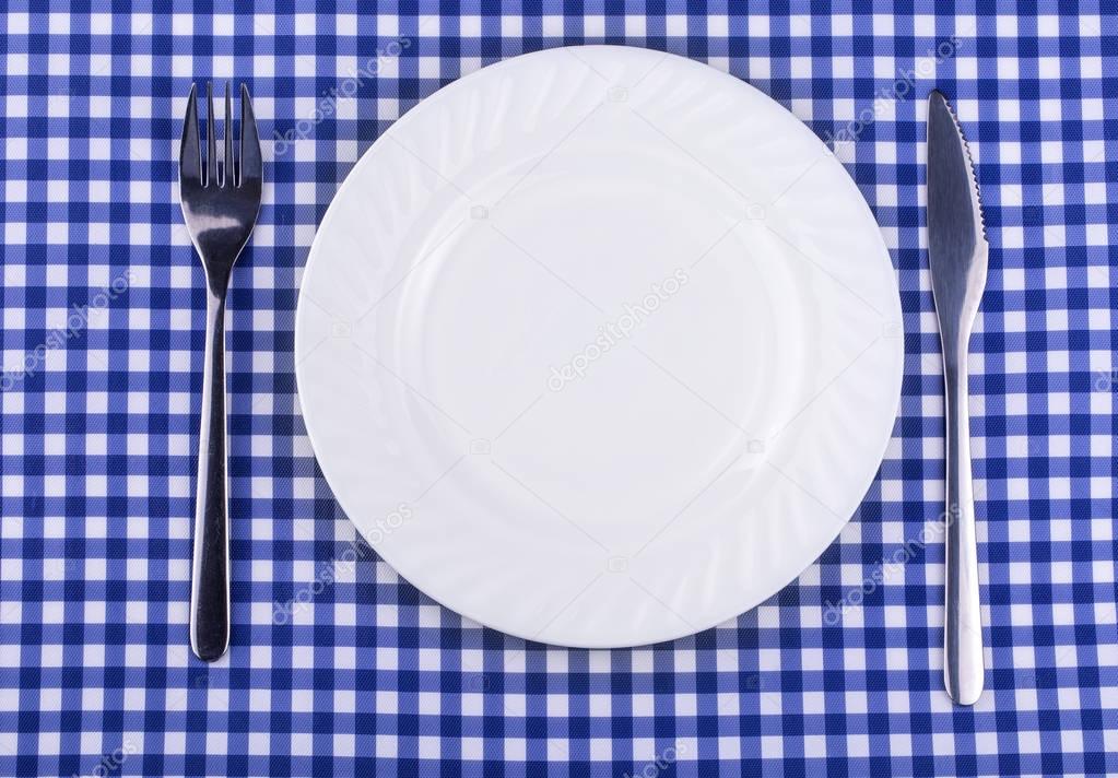 Empy plate and with a knife fork on the tablecloth in a cage