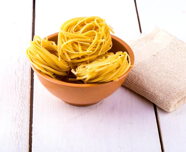 Italian pasta fettuccine nests in in a clay Cup and burlap, — Stock Photo, Image