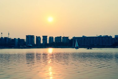 Günbatımı alacakaranlığı altında gölün yanındaki modern apartman binası. Arka planda su yansımaları olan bulutlu gökyüzü arkaplanı..