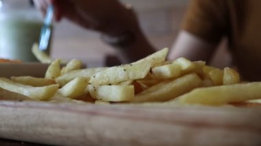 Lokantadaki masada tabaktan patates kızartması alan ellerin yakın çekimi. Fast food, sağlıksız yemek, insanlar ve abur cubur konsepti..