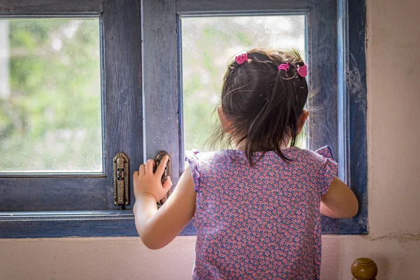 Little girl looks outside window