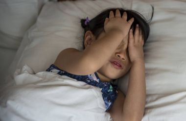 Yatakta, küçük Asyalı kız baş ağrısı eller yüzünde