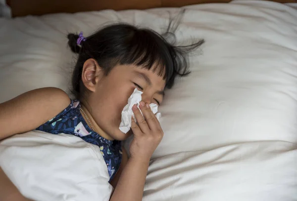 Pequeña chica asiática con frío soplando su nariz mocosa en la cama —  Fotos de Stock