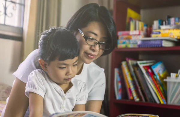 Азіатський матері прочитати книгу з дочкою в спальні — стокове фото