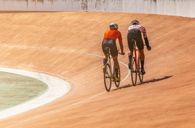 Arka tarafta bisiklet pistindeki iki bisikletçi birlikte hız trenine biniyor. Tayland 'da eski turuncu velodromda yarışmak. Sıcak bir günde yarışmadan önce profesyonel bisikletçiler birlikte pratik yaparlar. Metin için boşluk.