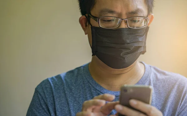 Portrait Asian man wears black medical mask and texting on smartphone, close up Asian man with eyeglasses, black short hair, eyes looking to smartphone, wears blue tshirt.