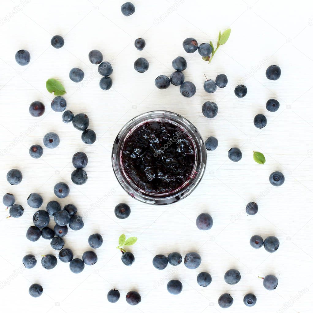 Open a jar of berry jam decorated with fresh berries and leaves forest blueberries top view