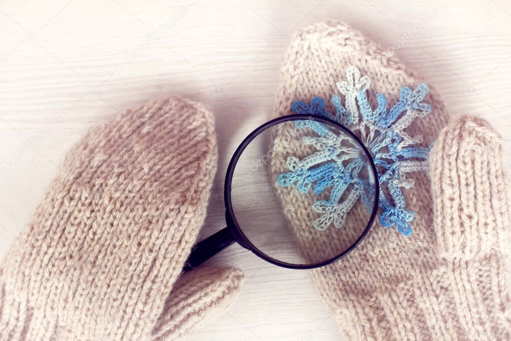 lying on a mitten a blue snowflake is viewed in a magnifying glass / winter which is knitted from a string
