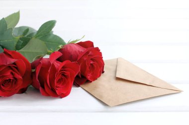 Kağıt zarf ve üç kırmızı gül açık masa manzaralı / düğün davetiyeli