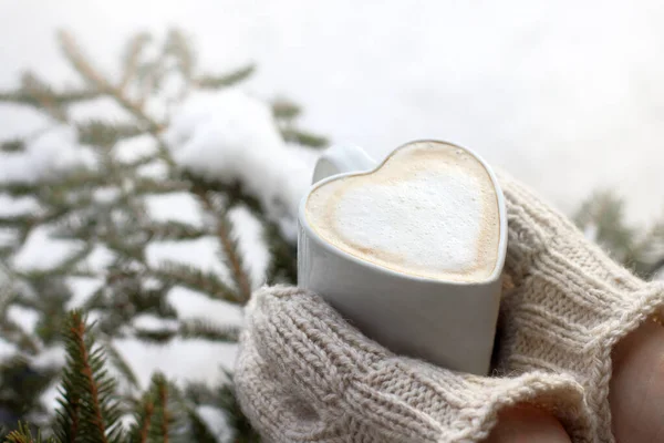 frothy coffee in a mug shaped like a heart, in the hands that are dressed in mittens .warming moments of winter holidays