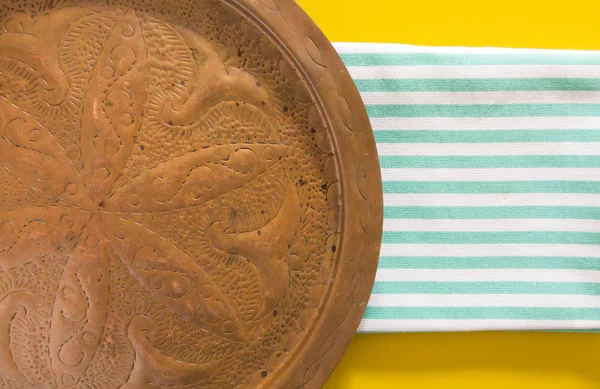 Old oriental copper dish on blue striped  folded towel and yellow background. — Stock Photo, Image
