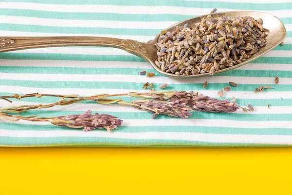 Cuchara antigua con lavanda seca sobre toalla doblada y fondo amarillo vivo . — Foto de Stock