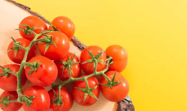 Montón de tomates rojos cereza con tallo en madera, sobre fondo amarillo vivo con espacio de copia — Foto de Stock