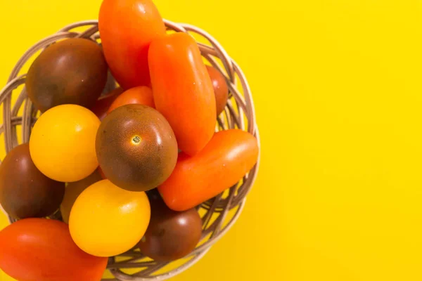 Tomates cereja coloridos em cesta de vime, em fundo amarelo vívido com espaço de cópia — Fotografia de Stock