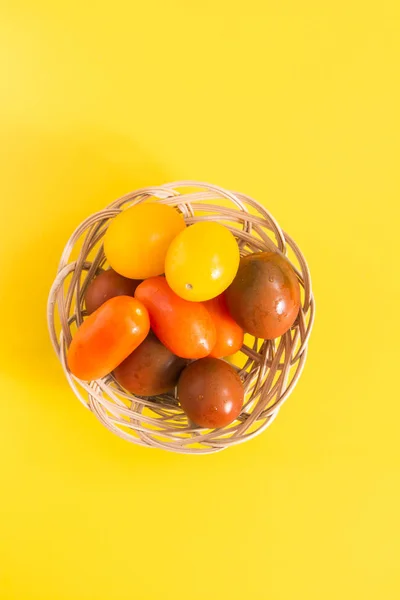 Kolorowe Pomidory czereśniowe w wiklinowym koszu, na żywy żółty tło — Zdjęcie stockowe