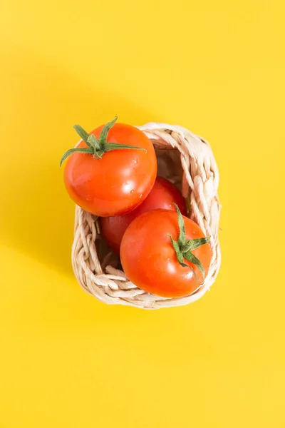 Tomates cereja vermelhos em cesta de vime, em fundo amarelo vívido — Fotografia de Stock