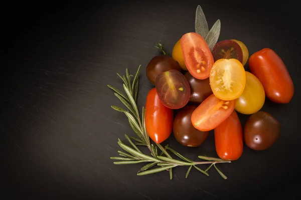 Colorful cherry tomatoes with herbs, on black background. — Stock Photo, Image