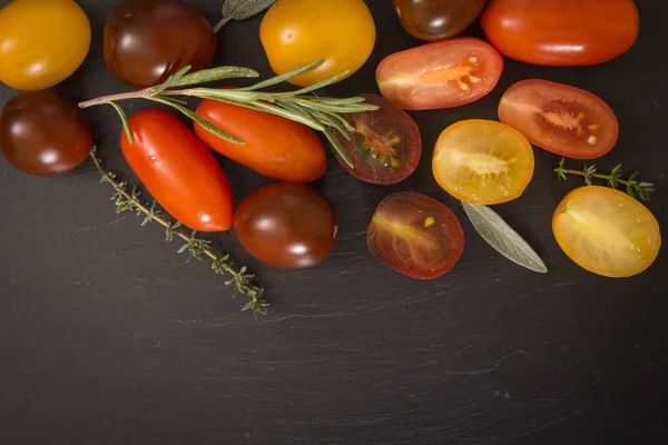 Bunte Kirschtomaten mit Kräutern, auf schwarzem Hintergrund. — Stockfoto